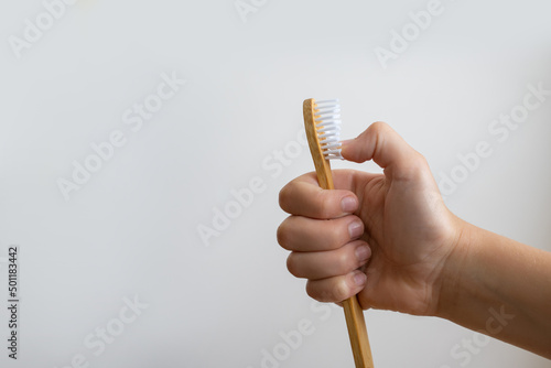 Child hand hold eco wooden toothbrush isolated on light background. Child dental hygiene, morning brushing, lifestyle, medical care. Copy space photo