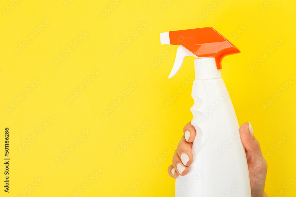 Cleaner's hand holding a chemical spray bottle. Empty space for text or logo on a yellow background. Early spring or regular cleaning. Cleaning and cleaning concept. flat lay Cleaner's hand holding a chemical spray bottle. Empty space for text or logo on a yellow background. Early spring or regular cleaning. Cleaning and cleaning concept. flat lay