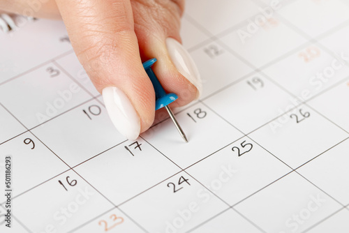 Blue Hand pin stuck on the 18 day of the month in the calendar, business concept. beautiful female hand fingers