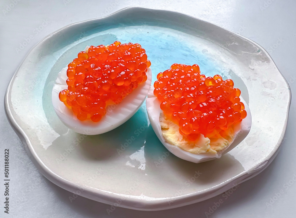 Halves of eggs with red salmon caviar traditional Russian snack served on white blue plate. Halves of eggs with red salmon caviar traditional Russian snack served on white blue plate.
