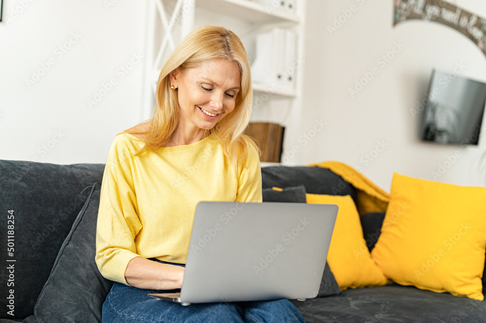 Modern mature 60s female enjoy leisure weekend at home, browsing wireless internet on computer gadget. Happy elderly woman sit relax on couch in living room, work on laptop, smiling Modern mature 60s female enjoy leisure weekend at home, browsing wireless internet on computer gadget. Happy elderly woman sit relax on couch in living room, work on laptop, smiling