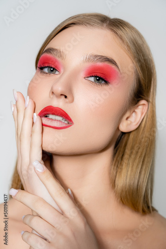 Young model with red makeup looking at camera isolated on grey.