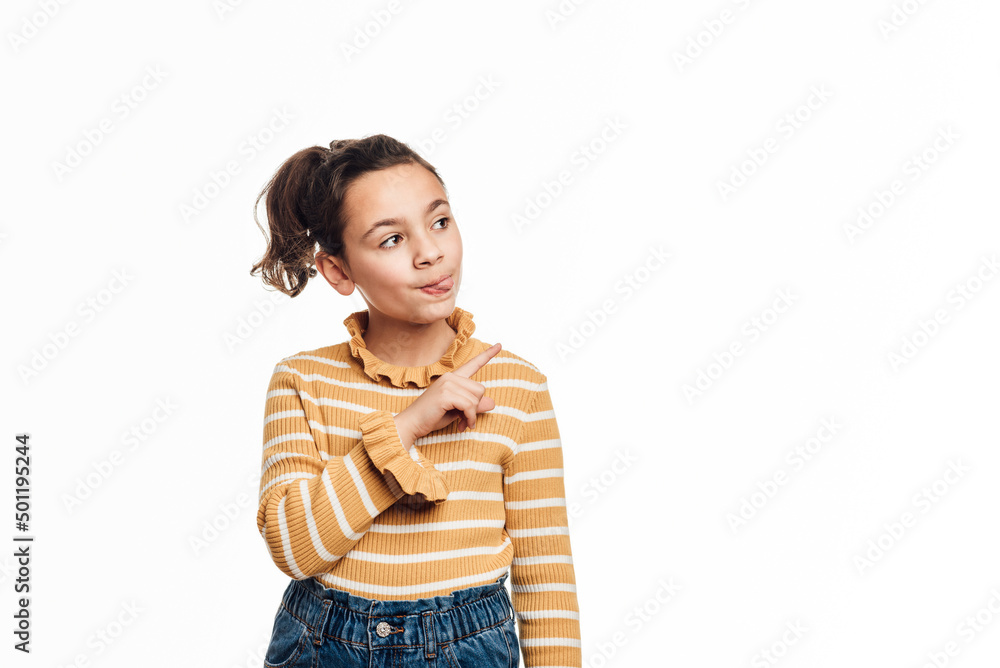 Young girl sticking tongue out and pointing to the side to show something while standing over an isolated background. Advertisement concept. Young girl sticking tongue out and pointing to the side to show something while standing over an isolated background. Advertisement concept.
