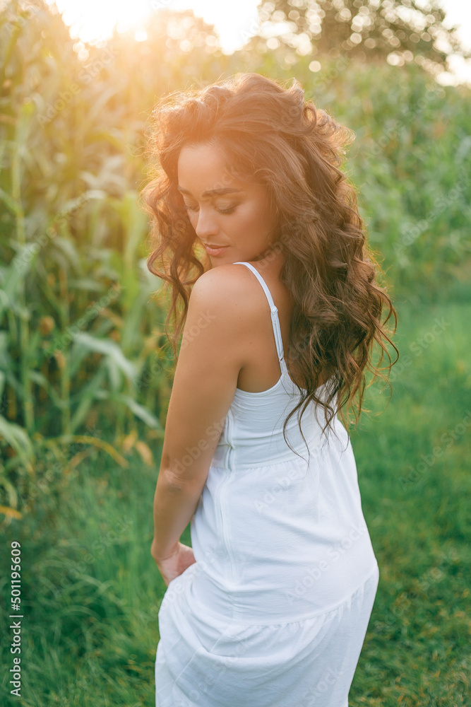 Portrait of a beautiful dark-haired curly young woman 30 years old in a white sundress in a summer field at sunset. Beautiful summer model. Portrait of a beautiful dark-haired curly young woman 30 years old in a white sundress in a summer field at sunset. Beautiful summer model.