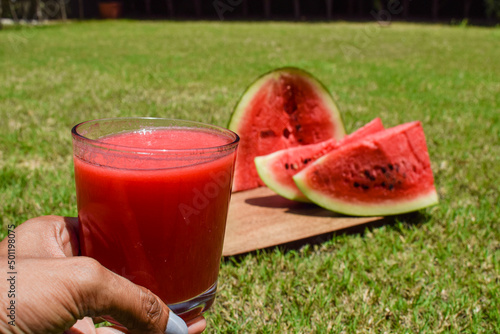 Girl holding Watermelon juice drink with freshly cut water melon fruit served in outdoor environment background. Fresh and delicious red colour Tarbooz ka Sharbat .Popular famous summer drinks photo