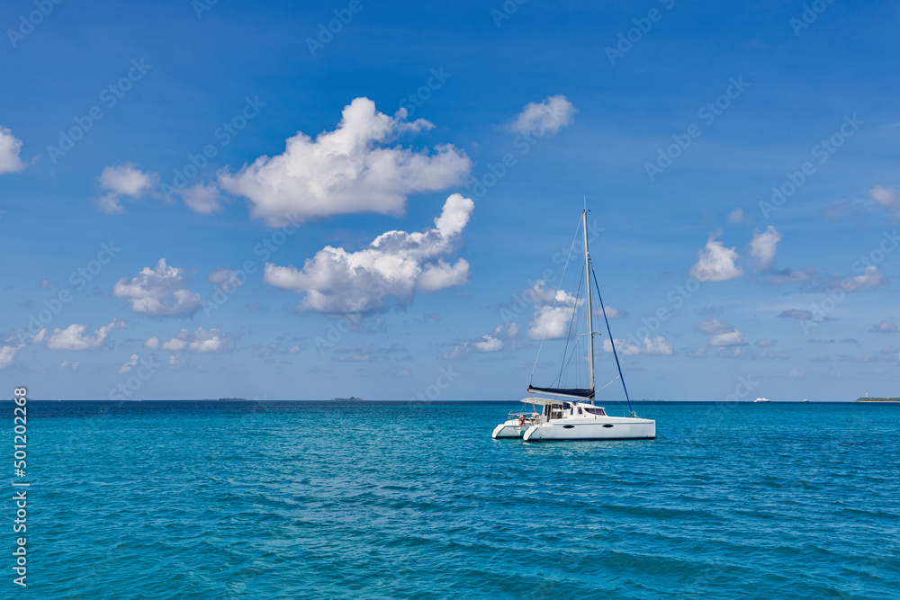 Naklejka premium Luxury yacht in open waters with beautiful clouds. Catamaran white sailboat in tropical ocean lagoon, sea horizon under sunny skyline. Idyllic outdoor sport and travel recreation landscape, seascape