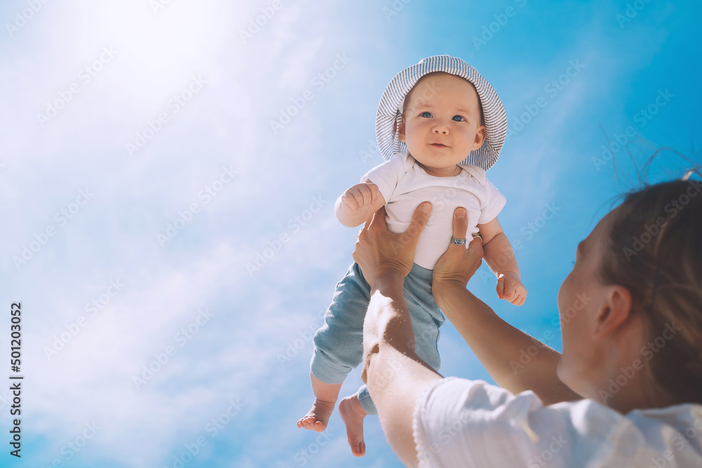 Mother throwing baby up against the blue sky. Happy family outdoors