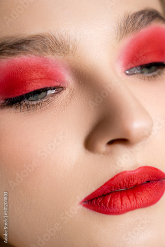 Close up view of young woman with red eye shadow and lips looking away.