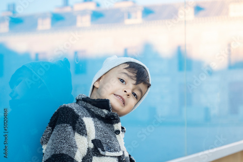 latin hispanic boy leaning on blue wall smiling