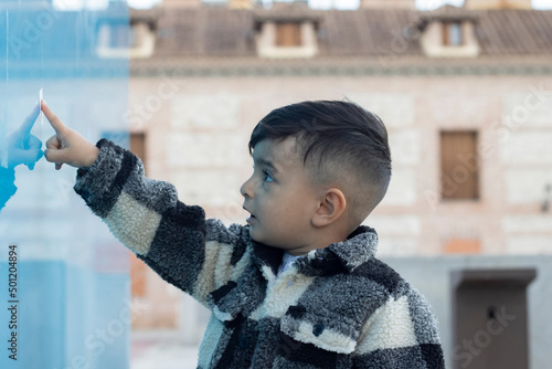 handsome and serious latin hispanic boy in casual clothes touches a blue wall