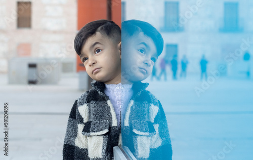 handsome boy is leaning against a blue glass wall where he reflects himself