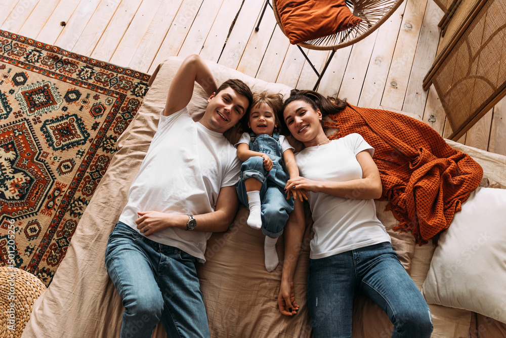 Happy family having fun in the bedroom while they lie on bed. Happy young family. Happy family laying on bed in bedroom with happy and smile, top view. Family relationships concept. Stock photo