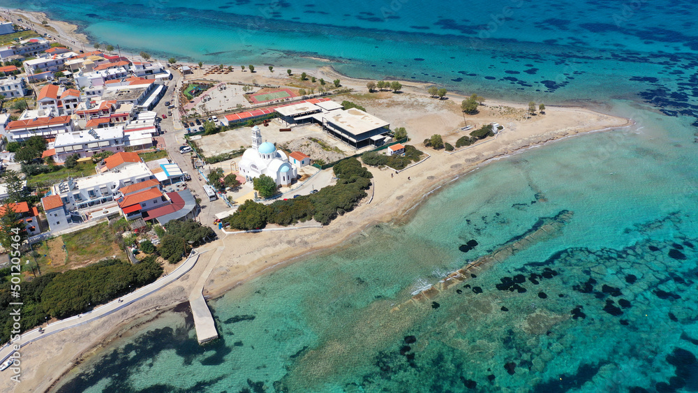 Aerial drone photo of iconic picturesque village, main port and beautiful turquoise beaches of Skala featuring landmark church of Agioi Anargiroi, Agistri island, Saronic gulf, Greece