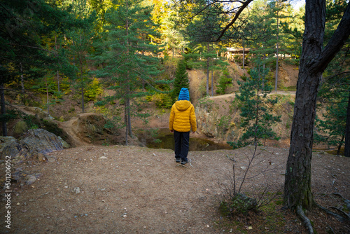 A little child is standing on the edge of a cliff, there is a small lake below