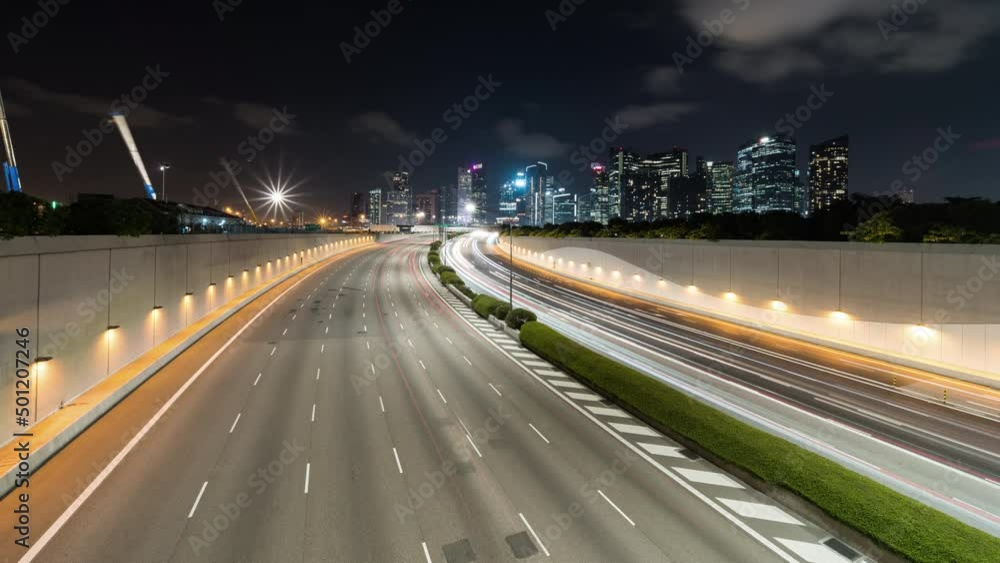 Time-lapse of car traffic transport on multiple lanes highway, financial district buildings, crane construction in Singapore at night. Asia transportation, commuter lifestyle, Asian city life concept Time-lapse of car traffic transport on multiple lanes highway, financial district buildings, crane construction in Singapore at night. Asia transportation, commuter lifestyle, Asian city life concept