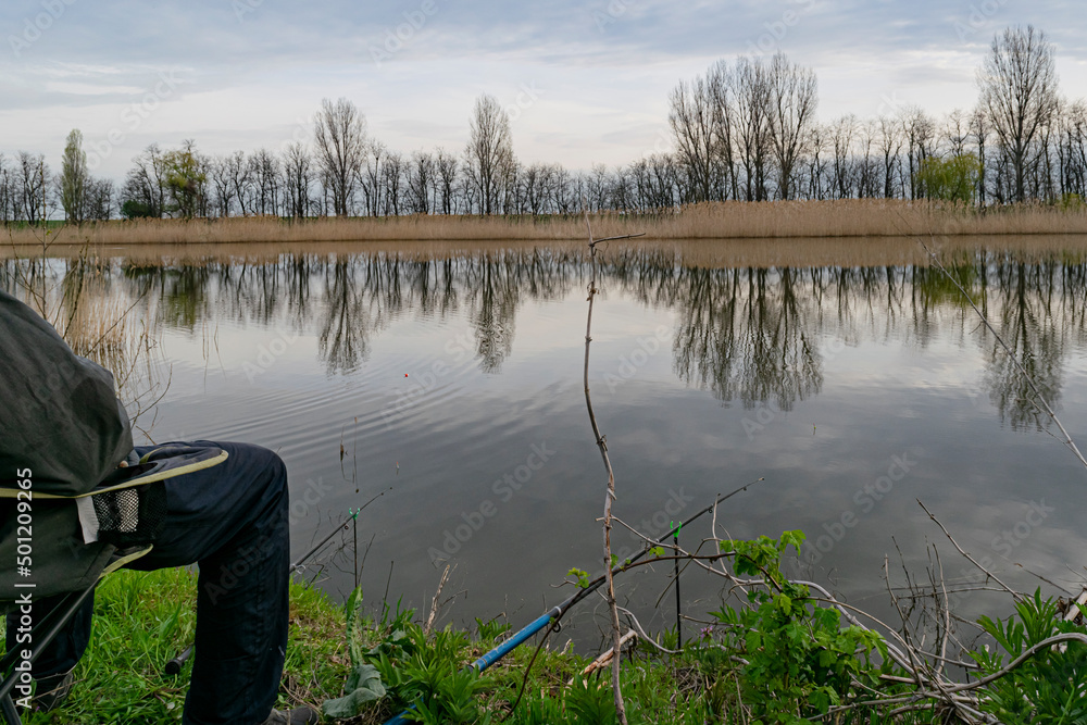 a man is sitting on the riverbank fishing with fishing rods.