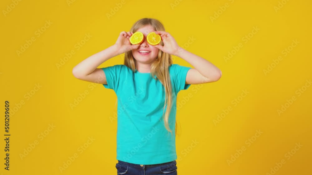 Studio Portrait Of Girl Holding Two Orange Halves In Front Of Eyes Against Yellow Background Studio Portrait Of Girl Holding Two Orange Halves In Front Of Eyes Against Yellow Background