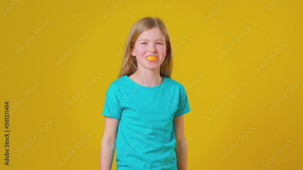 Studio Portrait Of Girl Using Orange Segment For Mouth And Teeth Against Yellow Background Studio Portrait Of Girl Using Orange Segment For Mouth And Teeth Against Yellow Background