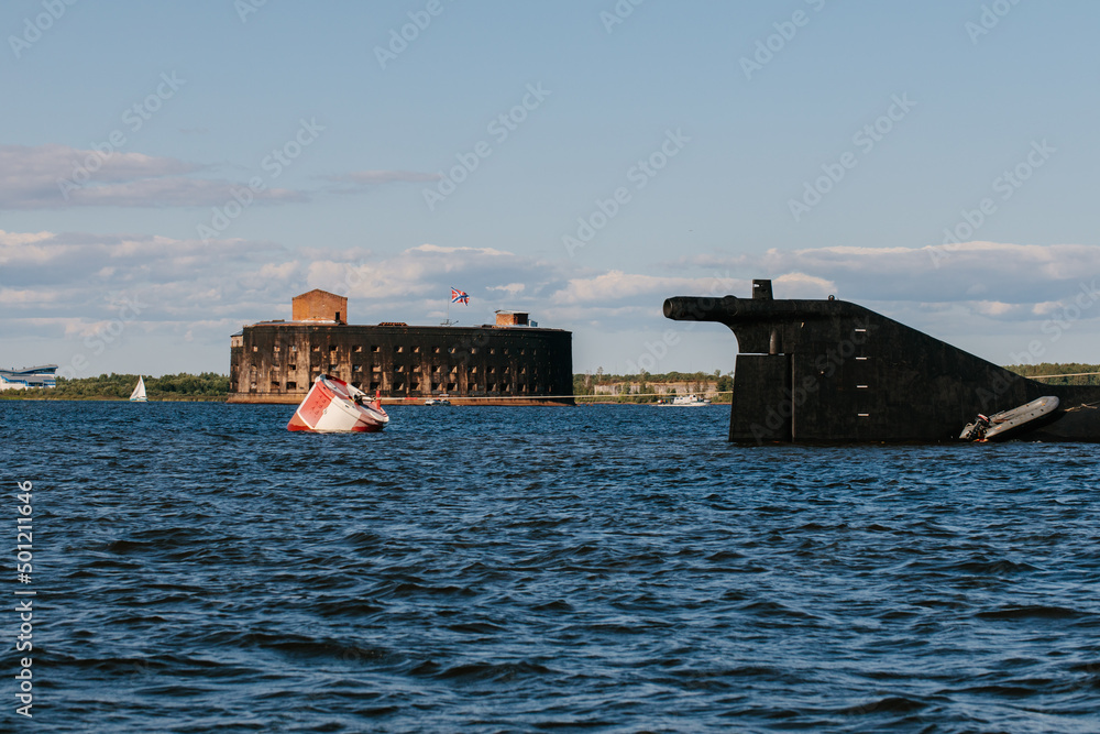 View from a boat on Fort Alexander the First in Kronstadt in the waters of the Gulf of Finland. The tail section of a nuclear-powered submarine. Island of forts