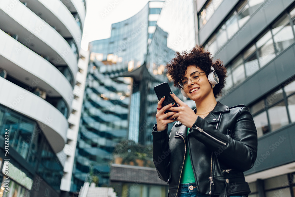 Fototapeta premium Woman walking in the city streets and using smartphone and headphones