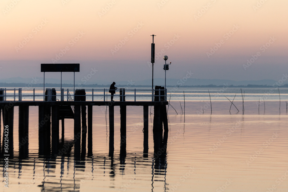 Man fishing on a pier on the lake at sunset Man fishing on a pier on the lake at sunset