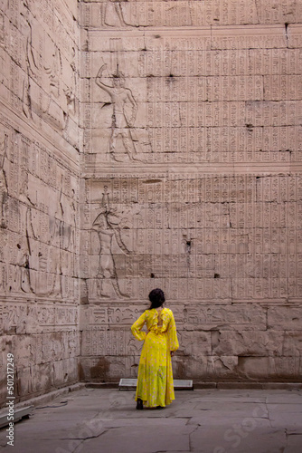 Woman in yellow dress looking at the hieroglyphs of the Temple of Edfu, Egypt