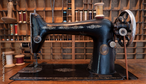 Old Edwardian sewing machine with hand operated mechanism. Behind it, an  up-cycled typesetters draw containing reels of cotton thread.