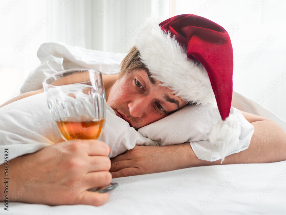 Man in Santa hat is trying to freshen the nip after alco party. He is  suffering of headache after New Year or Christmas celebration. Heavy  morning. Alcohol withdrawal. Worst hangover. Photos