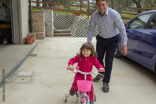 Young dad teaching his daughter to ride a bicycle in the backyard. Happy smiling family