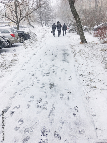 Three men walk down the street covered with snow. Footprints on snowy pavement. Winter in town.