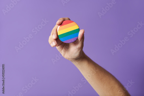 Hand raising a rainbow flag badge, symbol of support for the LGBT community.