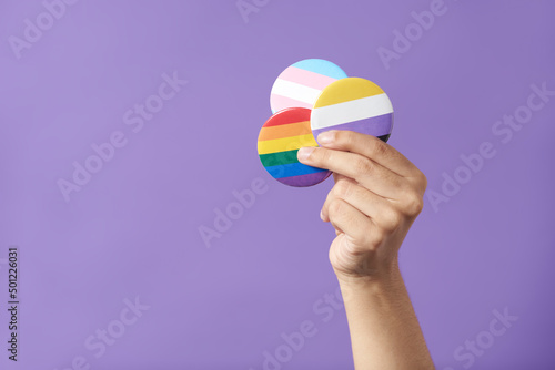 Hand raising three pins with rainbow, trans and non binary flags. LGBT pride. photo