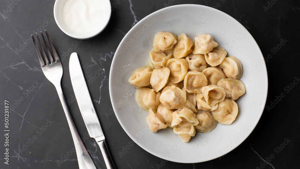 Meat dumplings, homemade russian pelmeni in bowl with sour cream isolated on black background