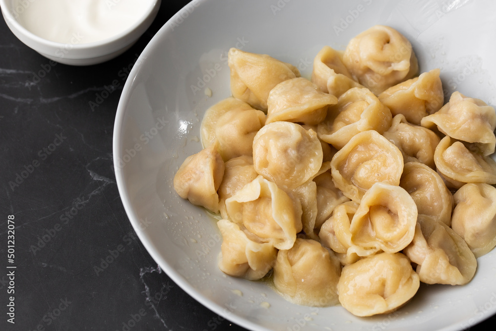 Meat dumplings, homemade russian pelmeni in bowl with sour cream isolated on black background