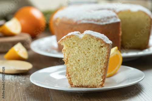 Close up piece of moist orange fruit cake on plate with orange slices on wooden table. Delicious breakfast, traditional English tea time. Orange cake recipe.
