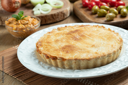 Chicken pie with cottage cheese, tomatoes, onion and olives on wooden table and white plate.