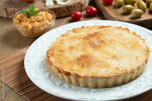 Chicken pie with cottage cheese, tomatoes, onion and olives on wooden table and white plate.