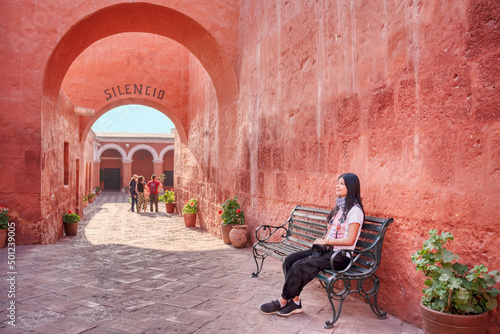 Joven turista sentada contemplando el arco de entrada del monasterio Santa Catalina en Arequipa, con personas de fondo