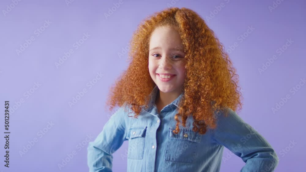 Studio Portrait Of Smiling Girl With Red Hair Standing Against Purple Background With Hands On Hips Studio Portrait Of Smiling Girl With Red Hair Standing Against Purple Background With Hands On Hips