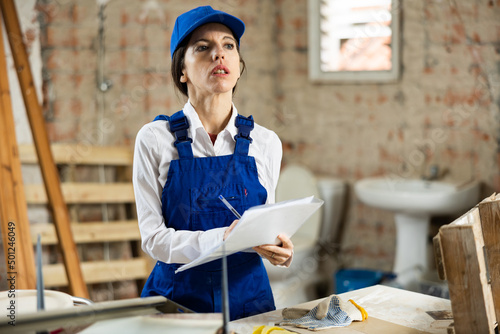 Woman worker filling documentation while standing in apartment during repair works