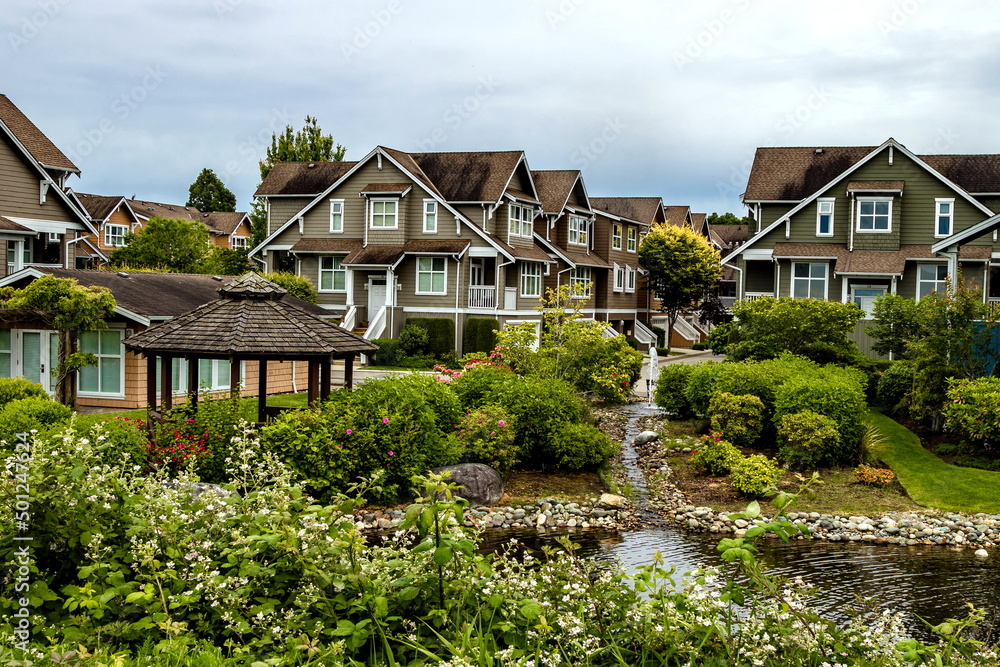 Residential District in Richmond City, a village of townhouses , green grass bushes and trees in the territory of residential complex, blue sky, Vanсouver, British Columbia Residential District in Richmond City, a village of townhouses , green grass bushes and trees in the territory of residential complex, blue sky, Vanсouver, British Columbia