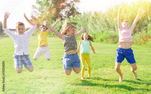 Children jumping and raising their hands up togeher outdoors.