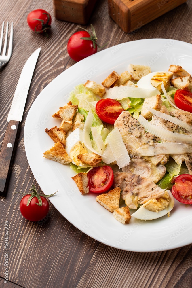 A Caesar salad with grilled chicken breasts, lettuce, croutons, eggs, cherry tomatoes, dressed with Parmesan cheese and sauce. On wooden background. A Caesar salad with grilled chicken breasts, lettuce, croutons, eggs, cherry tomatoes, dressed with Parmesan cheese and sauce. On wooden background.