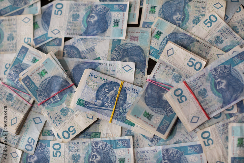 A file of banknotes lies on a scattering of fifty Polish zloty bills.