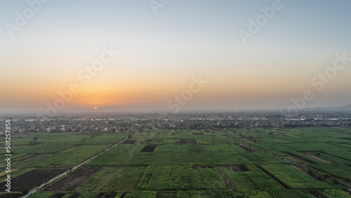 Dawn over the Nile Valley. The sun rises in a pinkish sky. Green cultivated plantations, village houses, riverbed are visible. View from above. Egypt. Luxor