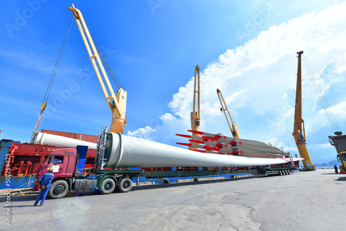 Large wind turbine rotor blades being unloaded from a ship onto a telescopic trailer for onward transportation by road to the construction site
