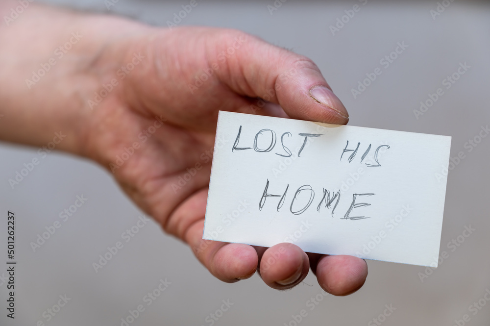 Lost his home. Words written in jagged letters. A man's hand holds a white paper rectangle with text against a gray background Lost his home. Words written in jagged letters. A man's hand holds a white paper rectangle with text against a gray background