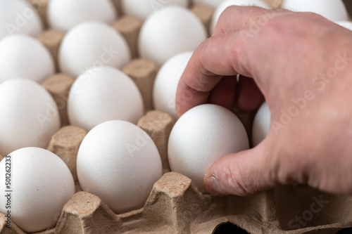 A man takes a chicken egg from a cardboard tray. Adult male holding a white raw egg. Open recycled tray.