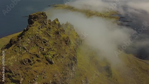 Aerial dolly in of verdant steep hills covered in clouds next to the sea, in Djúpivogur small town near Iceland fiords at daytime photo