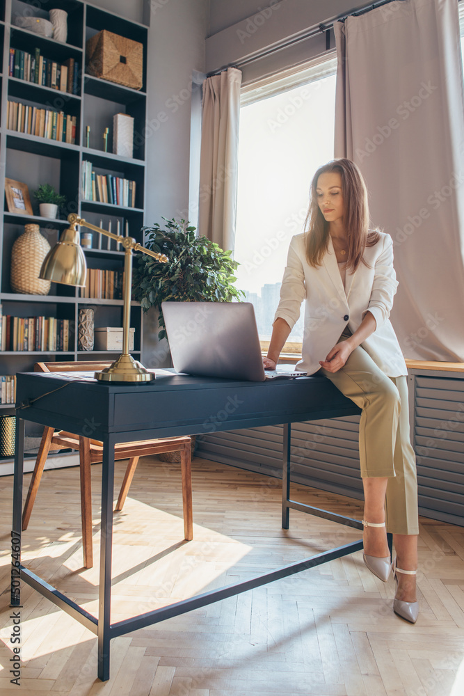 Woman sits on the edge of work table and looks at laptop screen. Woman sits on the edge of work table and looks at laptop screen.